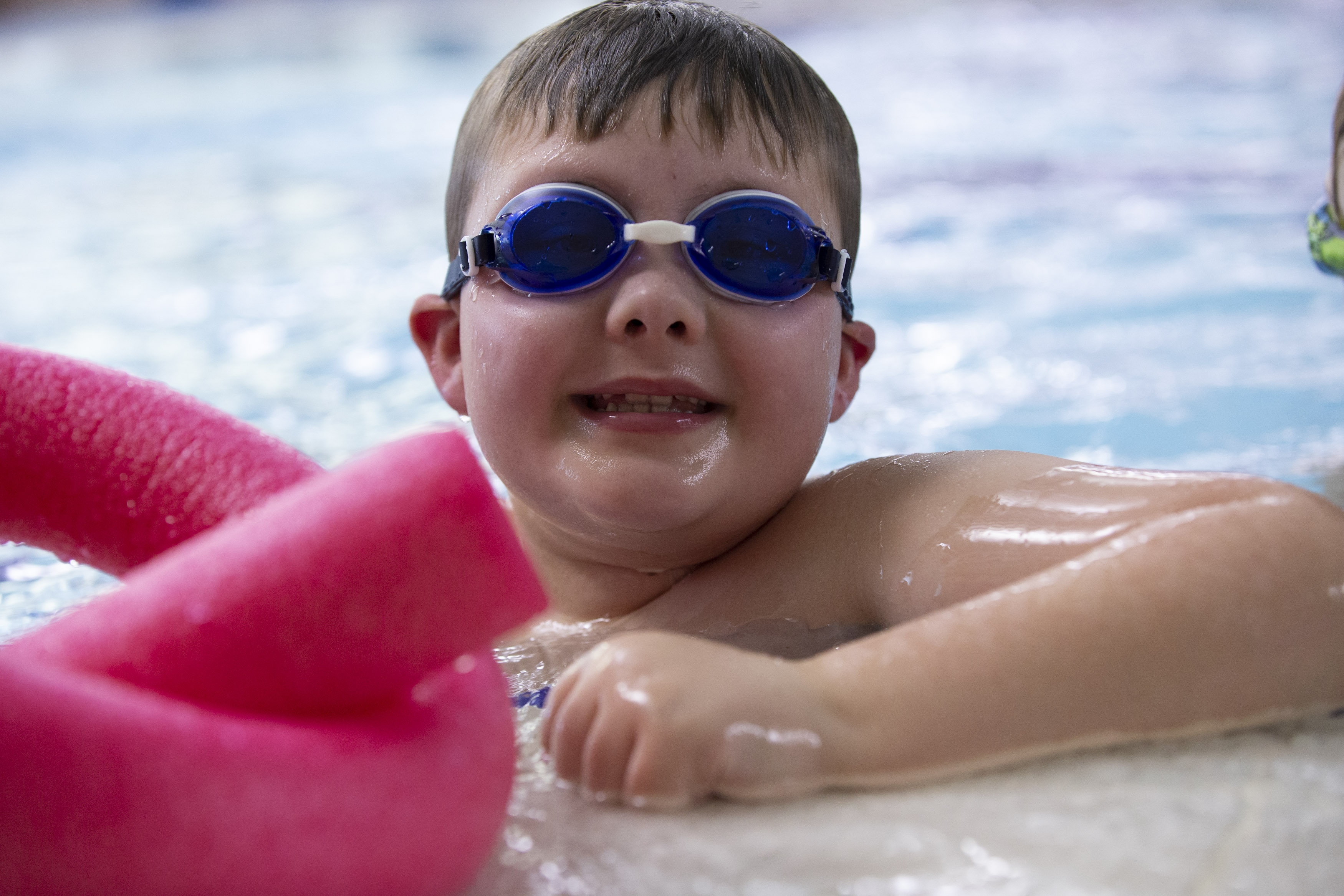Young Boy in blue goggles smiles at the side of the pool