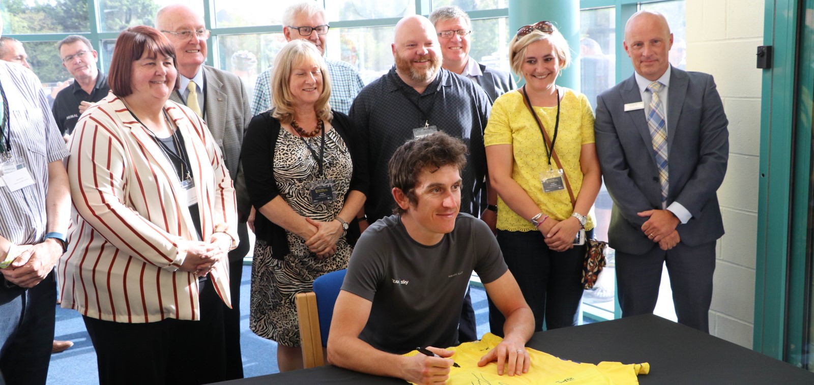 Cyclist Geraint Thomas sat a table with a line of people behind him