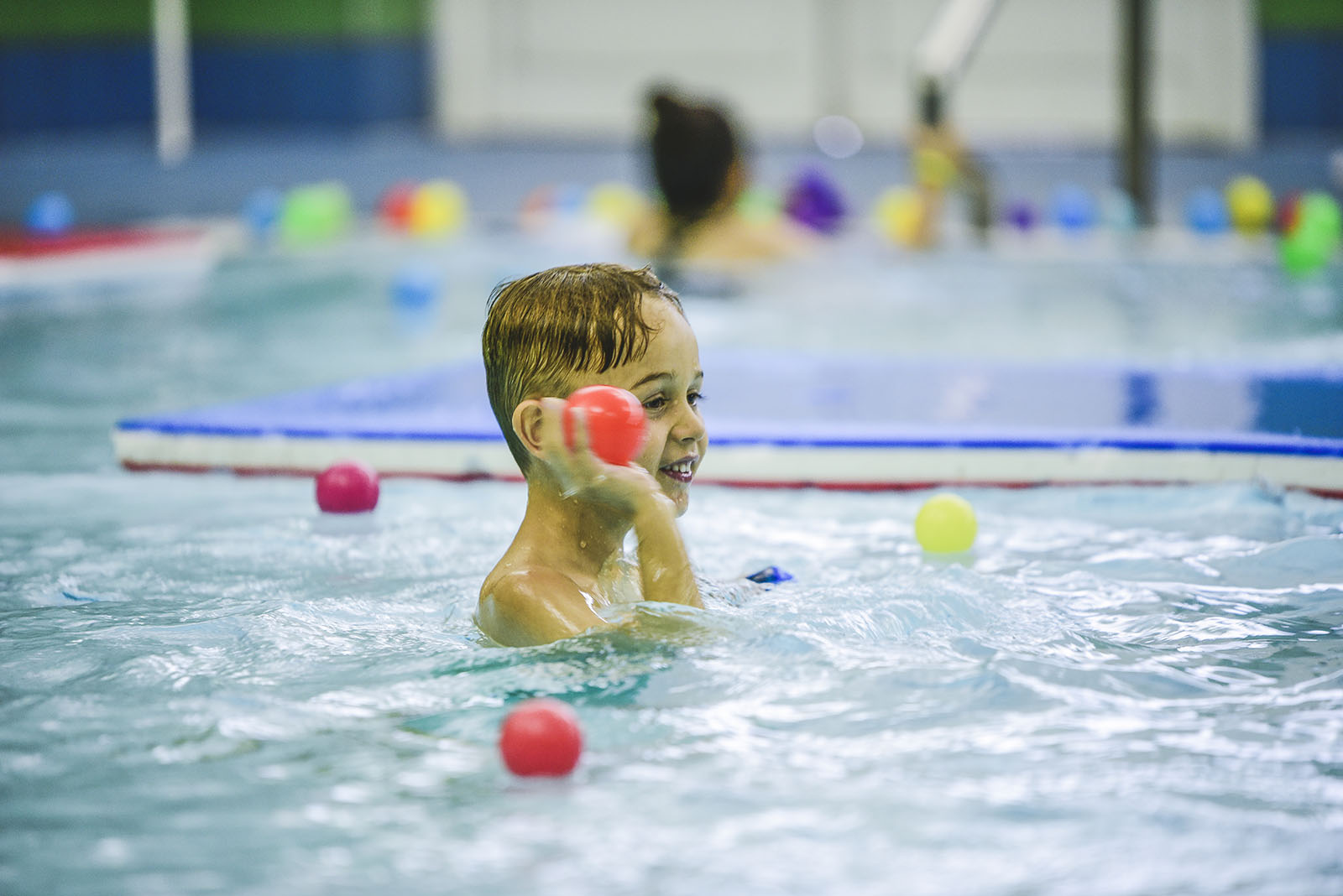 young boy playing in a swimming pool with water float balls