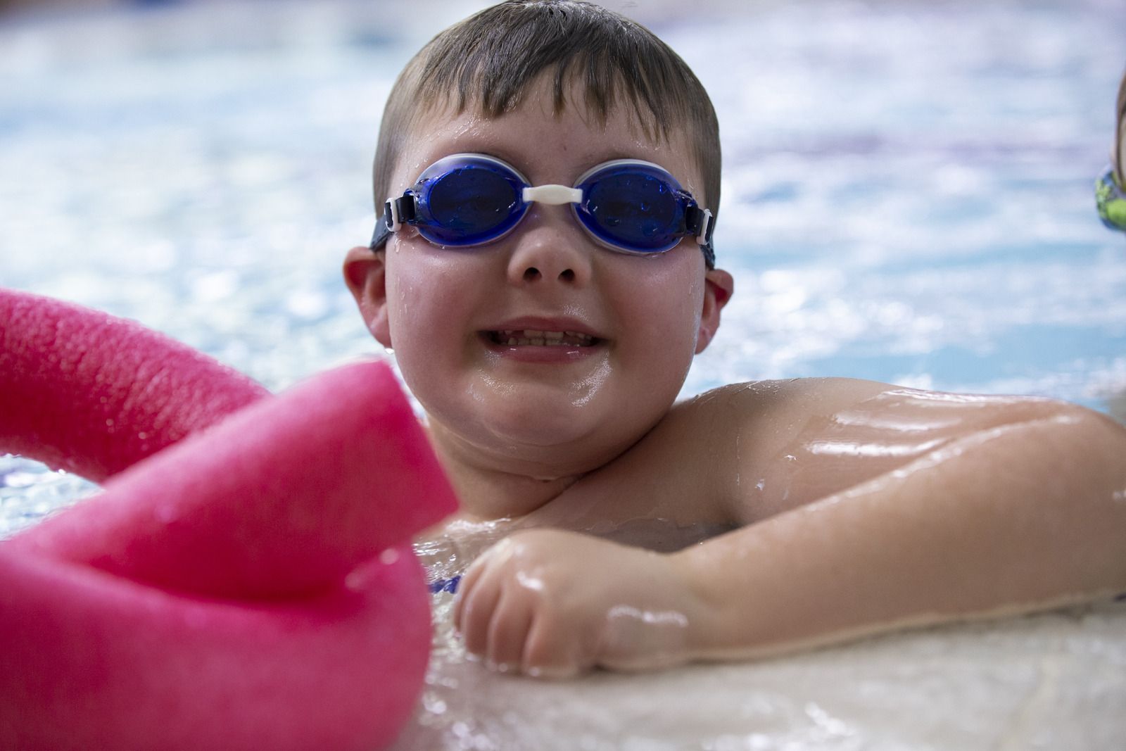 Young Boy in blue goggles smiles at the side of the pool Young Boy in blue goggles smiles at the side of the pool