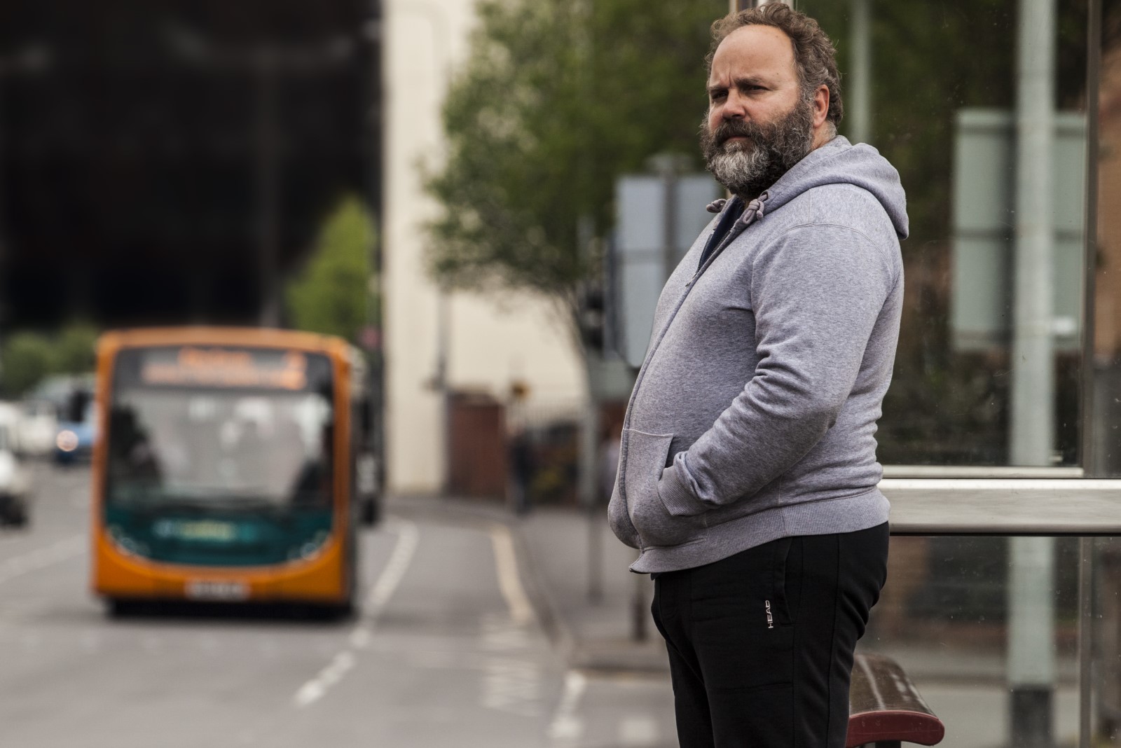 Man stood at a bus stop in a grey hoodie.jpg