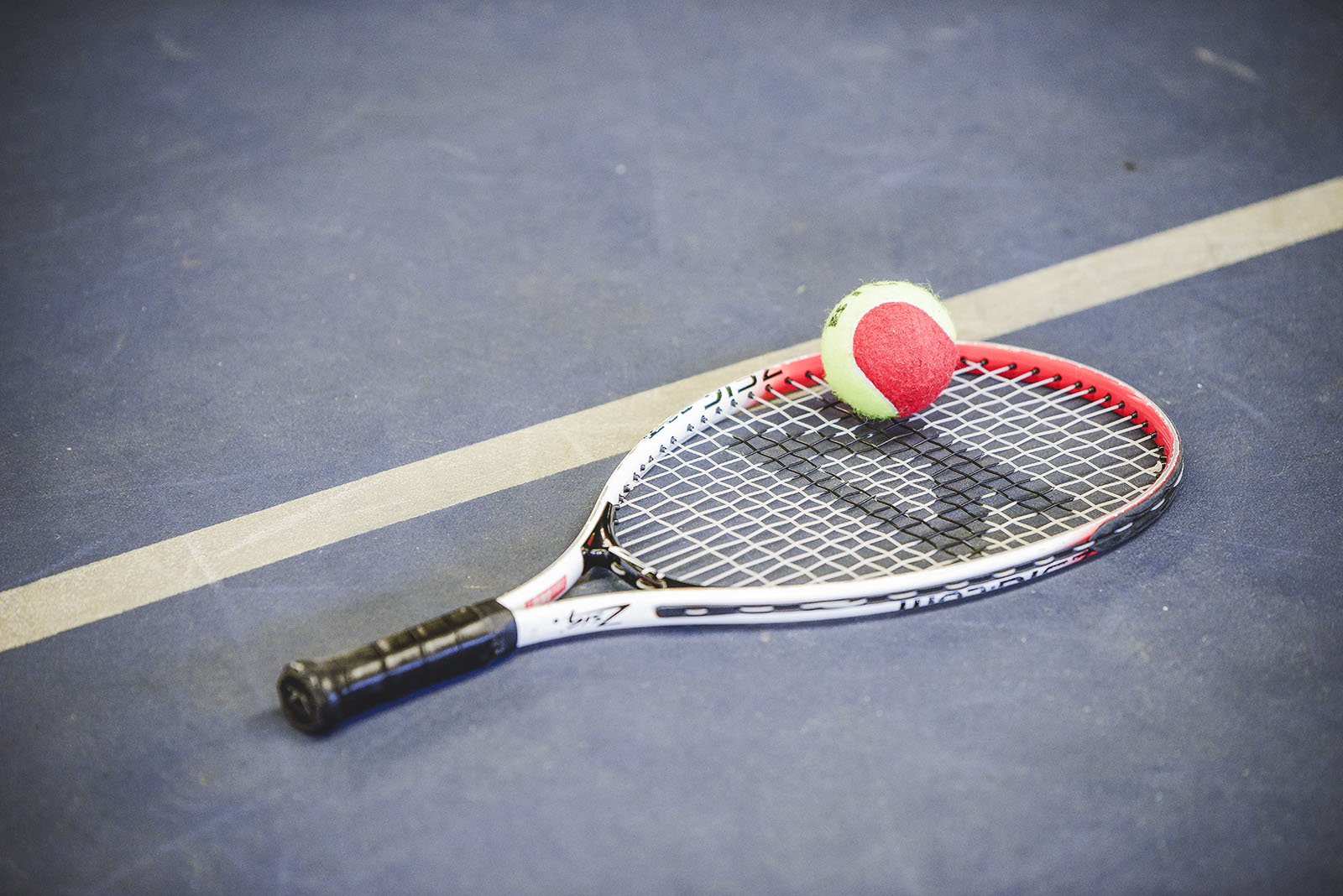 Red and yellow tennis ball sitting on a raquet