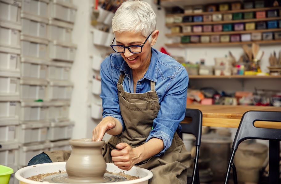 Grey haired lady in apron working at a potters wheel