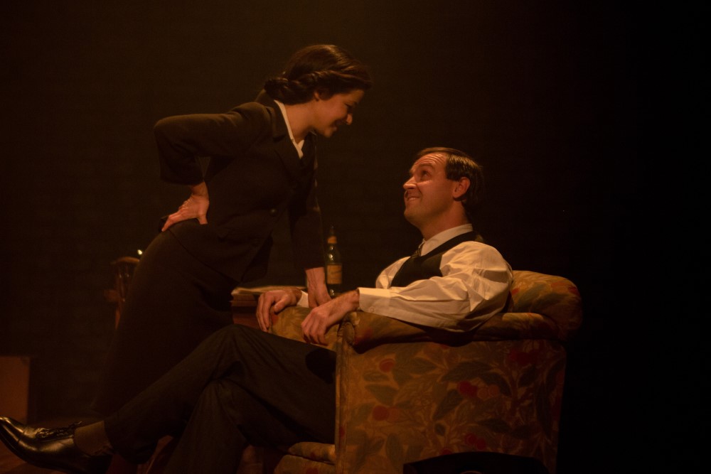 Promotion image for theatre show Nye & Jennie. Lady leans over man sitting in arm chair Promotion image for theatre show Nye & Jennie. Lady leans over man sitting in arm chair
