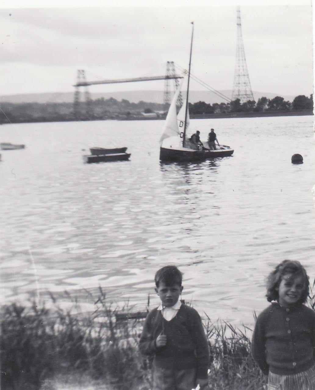 Black and white image of two children in front of water with the transporter bridge in the background