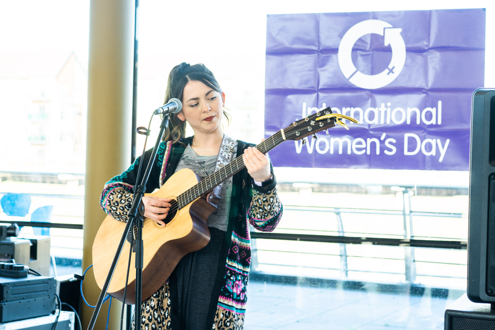 lady with a guitar performing in from of a purple IWD flag